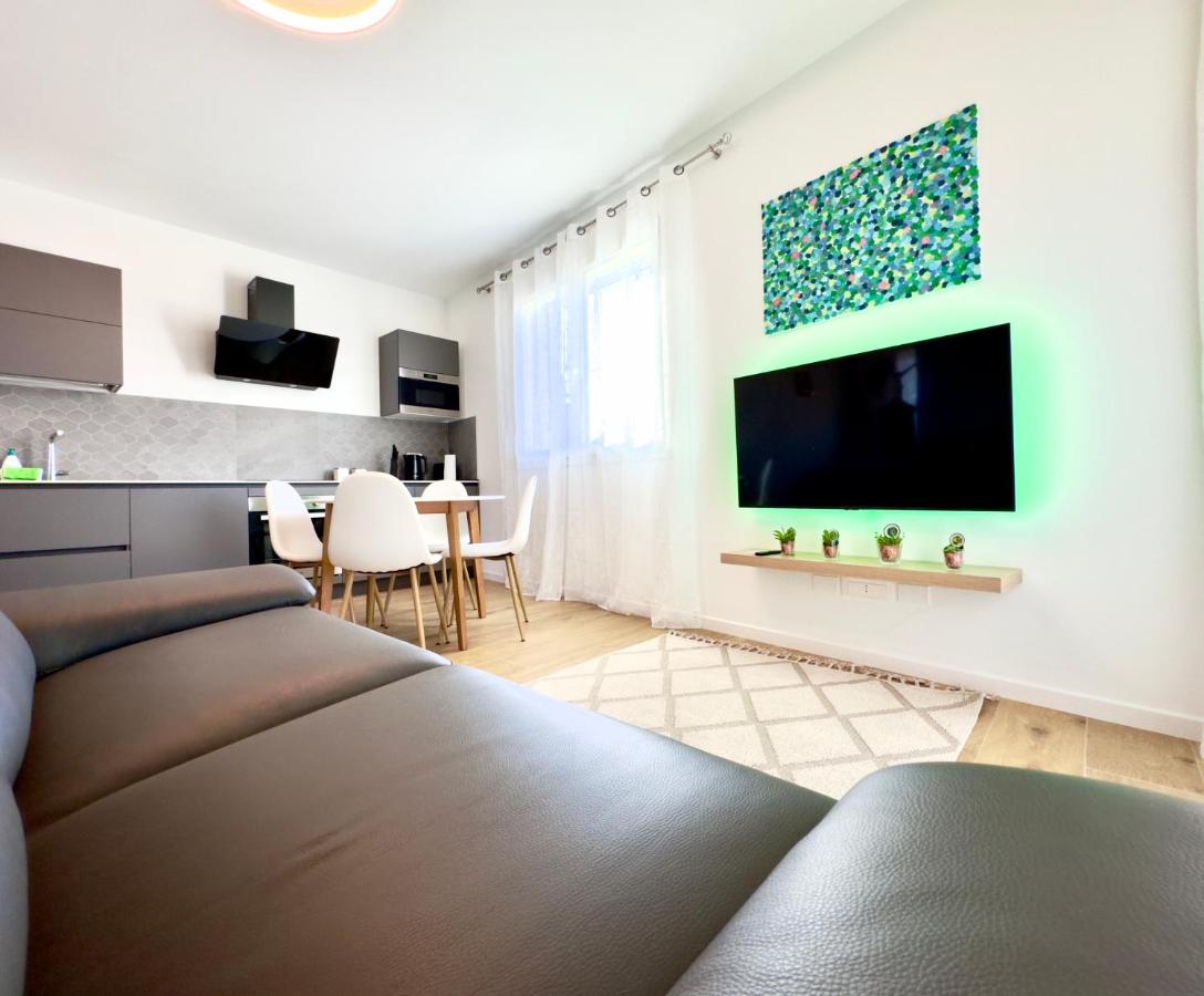 Soggiorno con divano grigio, smart TV con luce LED verde e cucina sullo sfondo
